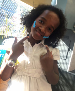 Smiling girl. Her fingers and blue arrows on her face point at her mouth.