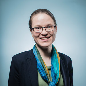 Photo of Katy, a woman with glasses wearing a black jacket and a bright turquoise scarf