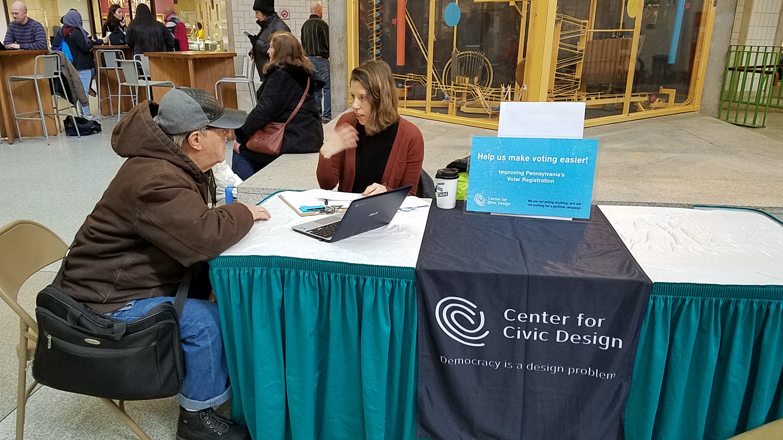 Two people are sitting at a table outside have a conversation about civic design.