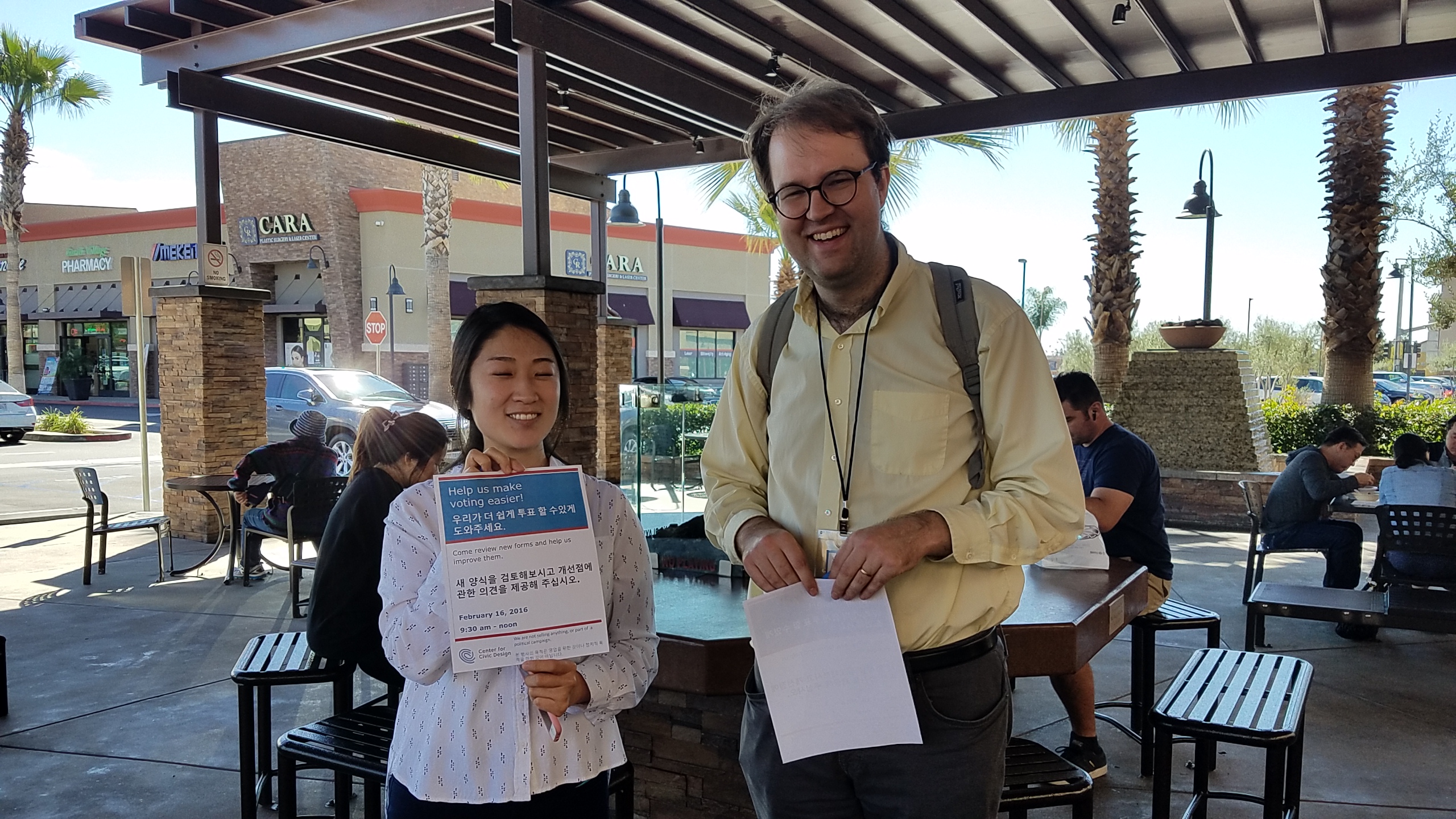 Two people are standing together holding up papers. One of them is holding a flyer in both English and Chinese
