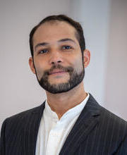 Photo of Nick, a man with short hair and beard, wearing a chack and a collarless shirt.